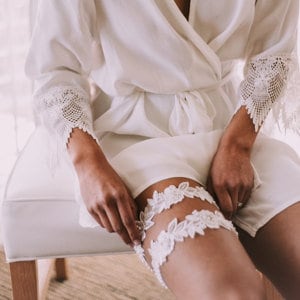May include: White lace garter with floral details, worn on a leg.