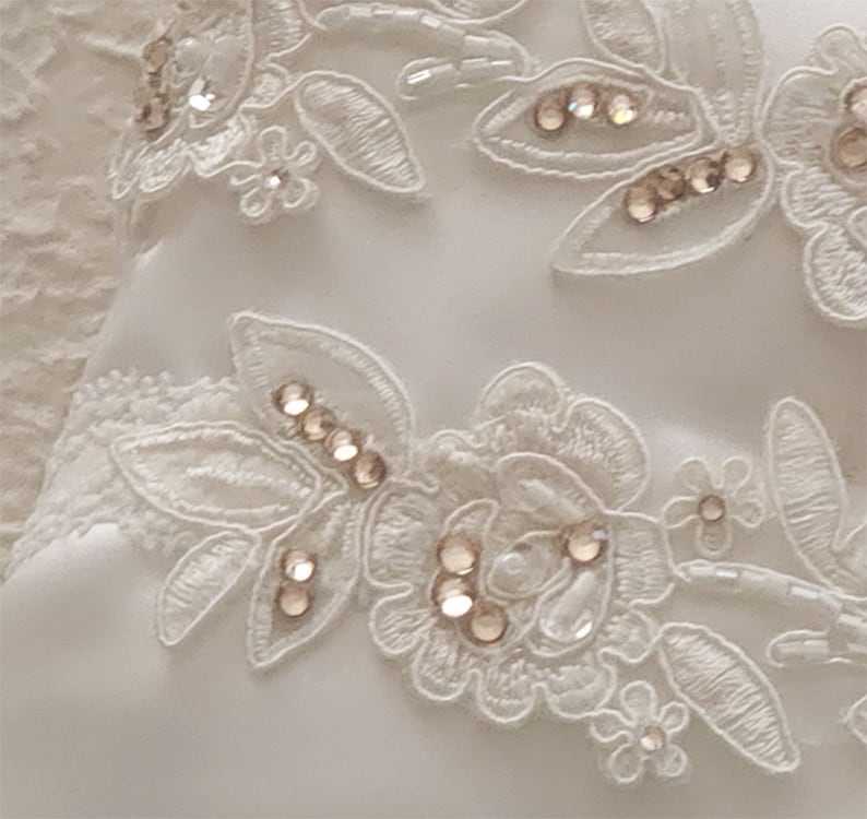 May include: White lace fabric with delicate floral patterns and small, clear rhinestones.