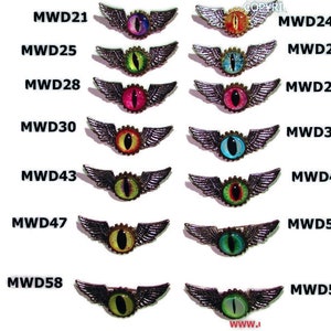May include: A collection of steampunk-style eye brooches with metal wings and gear accents. Each brooch features a different colored eye, including purple, orange, green, pink, and blue. The brooches are displayed against a white background.