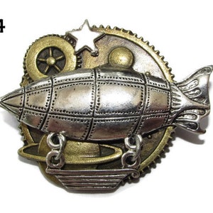 Könnte beinhalten: Eine silberne und bronzene Steampunk-Anstecknadel mit einem kleinen Luftschiff mit einem Stern und Zahnrädern. Das Luftschiff hat ein detailliertes Design mit einer strukturierten Oberfläche.