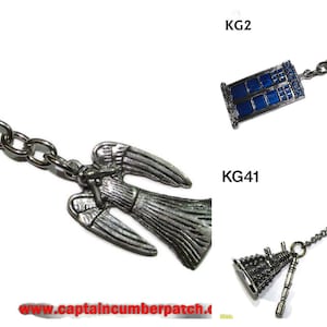 Könnte beinhalten: Drei silberne Schlüsselanhänger mit verschiedenen Anhängern. Der erste Schlüsselanhänger hat einen silbernen Engelsanhänger. Der zweite Schlüsselanhänger hat einen blauen und silbernen TARDIS-Anhänger. Der dritte Schlüsselanhänger hat einen silbernen Dalek-Anhänger. Die Schlüsselanhänger befinden sich alle auf einem weißen Hintergrund.