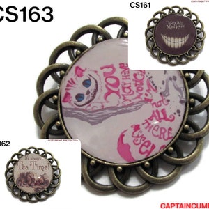 May include: Three round, bronze-colored, decorative brooches with glass cabochons. The first brooch features a Cheshire Cat from Alice in Wonderland with the text "You may have noticed... not all there... yet". The second brooch features a smiling Cheshire Cat with the text "We're All Mad Here". The third brooch features a scene from Alice in Wonderland with the text "It's always Tea Time!"