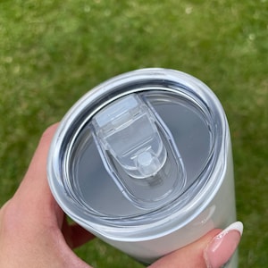 May include: White stainless steel tumbler with a clear lid. The lid has a small, clear handle.