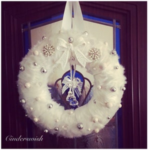 A Cream faux fur luxury wreath with silver and white mini baubles within the fur finished off with a chandelier glass ornament in the middle.