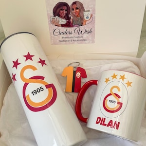 May include: A white gift box with a white tumbler, a white mug, and a red and yellow jersey keychain. The tumbler and mug feature a red and yellow logo with the text "1905" and five stars. The mug also has the name "DILAN" printed on it.