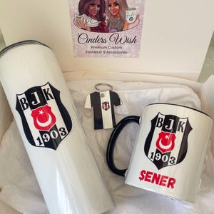May include: A white gift box with a white mug, a white tumbler, and a keychain with a black and white jersey. The mug and tumbler have a black and white logo with the text "BJK 1903" and the mug also has the text "SENER".