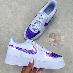 May include: White leather low-top sneakers with a purple rhinestone swoosh and toe. The word "AIR" is printed on the side of the shoe.