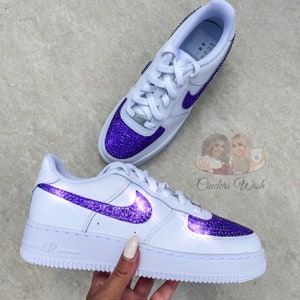 May include: White leather low-top sneakers with a purple rhinestone swoosh and toe. The word "AIR" is printed on the side of the shoe.