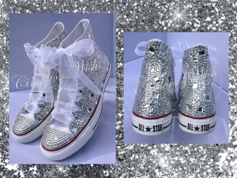 May include: White high-top sneakers covered in silver glitter and rhinestones. The sneakers have white laces and a white ribbon tied around the ankles. The words "All Star" are printed on the back of each shoe.
