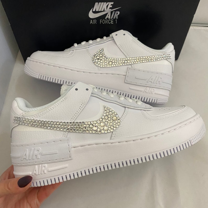 Puede incluir: Zapatillas bajas de cuero blanco con suela de goma blanca. El swoosh de Nike est&aacute; adornado con diamantes de imitaci&oacute;n.