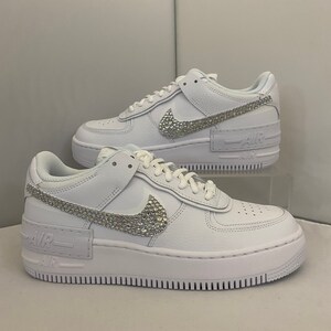 Puede incluir: Zapatillas bajas de cuero blanco con suela de plataforma. El swoosh de Nike est&aacute; adornado con pedrer&iacute;a. El texto "AIR" est&aacute; impreso en el lateral de la zapatilla.