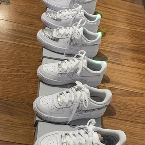 Puede incluir: Una fila de zapatillas blancas de cuero con pedrer&iacute;a en los laterales y cordones. Las zapatillas est&aacute;n expuestas en una tienda.