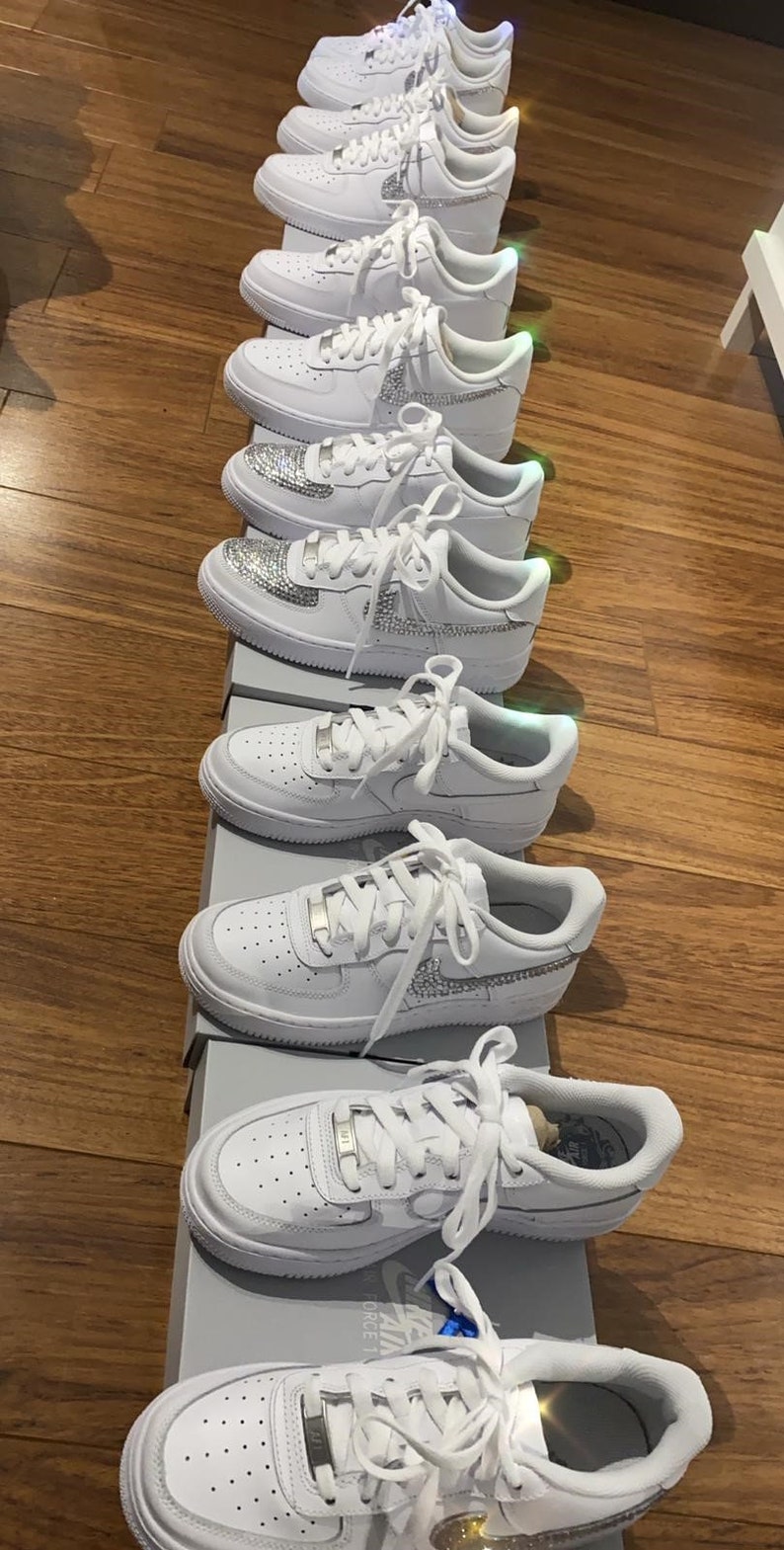 Puede incluir: Una fila de zapatillas blancas de cuero con pedrer&iacute;a en los laterales y cordones. Las zapatillas est&aacute;n expuestas en una tienda.