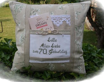Puede incluir: Un cojín decorativo beige con un estampado floral y un bolsillo. El bolsillo contiene una tarjeta que dice "Sweet Dreams" y un mensaje bordado que dice "Lotte Alles Liebe zum 70. Geburtstag". El cojín tiene detalles de encaje y cinta.