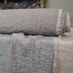 Puede incluir: Primer plano de una tela texturizada de color marrón claro doblada por la mitad. La tela tiene un aspecto ligeramente arrugado y un brillo sutil.