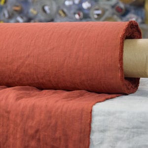 May include: A roll of rust-colored linen fabric. The fabric is woven with a subtle texture and is rolled on a cardboard tube.