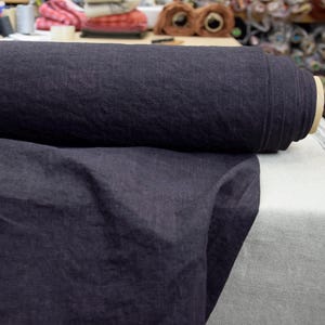 Könnte beinhalten: Eine Rolle dunkelblauen Leinenstoffes. Der Stoff ist weich und hat eine natürliche Textur.