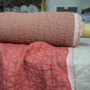 May include: A roll of pink and brown patterned fabric with a textured surface. The fabric has a subtle geometric design.