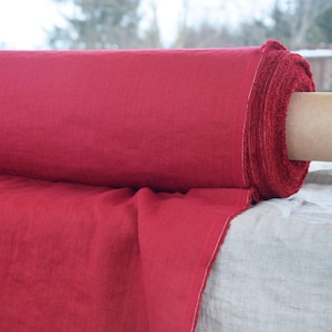 Puede incluir: Un rollo de tela de lino roja. La tela está doblada y enrollada, con el extremo del rollo visible. La tela es de color rojo intenso y tiene una superficie ligeramente texturizada.