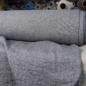 Könnte beinhalten: Eine Rolle grauer Stoff mit einem weißen Rautenmuster. Der Stoff ist in der Mitte gefaltet und die Rolle liegt auf einer weißen Oberfläche.