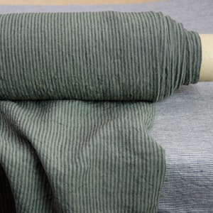 Pode incluir: Um rolo de tecido verde escuro com finas listras brancas. O tecido tem uma aparência texturizada, ligeiramente enrugado.