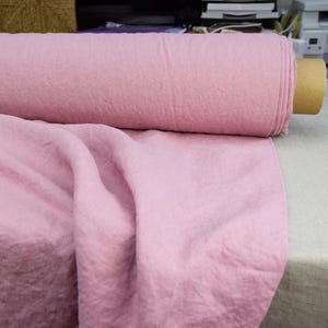 Puede incluir: Un rollo de tela rosa claro, con una textura suave y arrugada. Parte de la tela est&aacute; enrollada, el resto drapeada. El material parece ser de peso medio, adecuado para diversos proyectos de costura y manualidades.