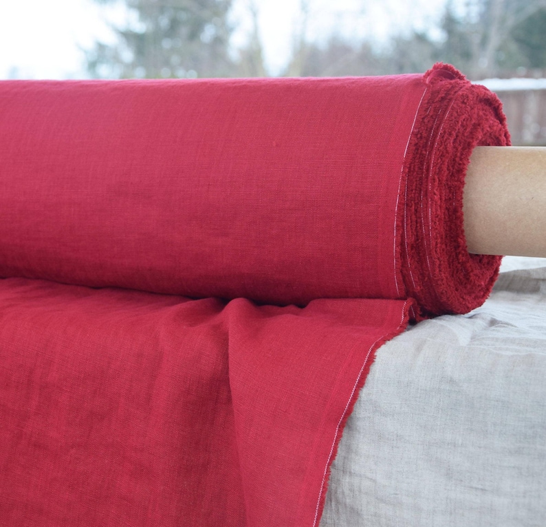 May include: A roll of red linen fabric. The fabric is folded and rolled up, with the end of the roll visible. The fabric is a deep red color and has a slightly textured surface.