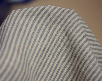 May include: Close-up of a folded fabric with a blue and white striped pattern. The fabric appears to be linen or a similar material, with a slightly textured surface. The stripes are evenly spaced and run diagonally across the frame.
