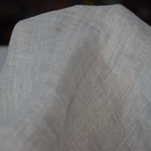 May include: A close-up of a light gray fabric with a textured weave. The fabric is soft and drapes nicely.