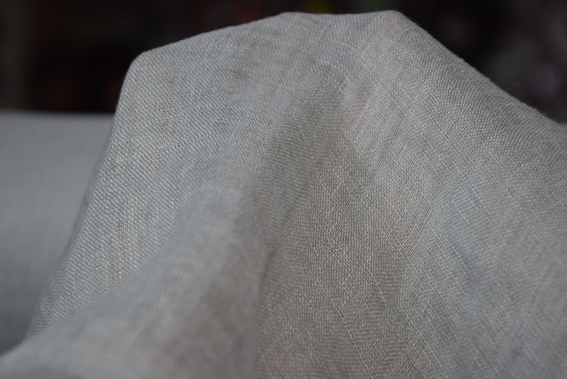 May include: A close-up of a light gray fabric with a textured weave. The fabric is soft and drapes nicely.
