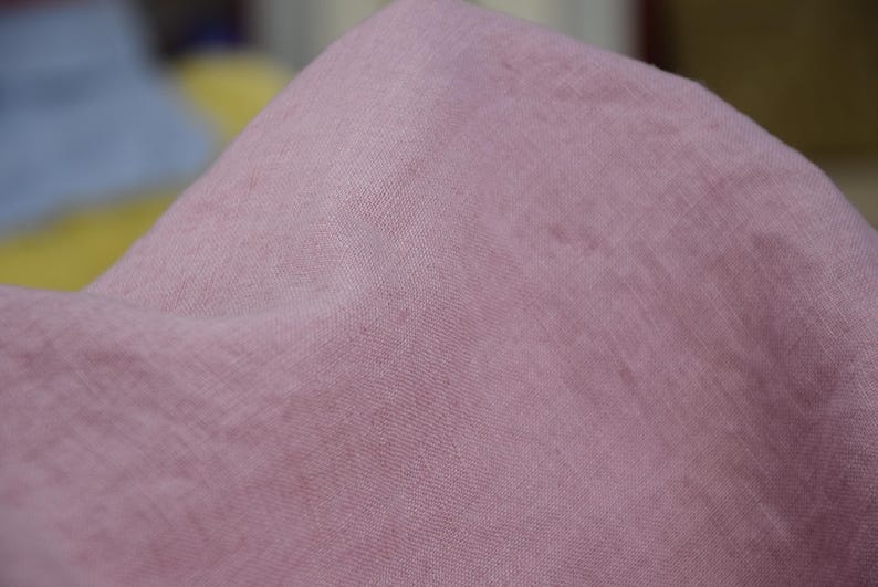 Puede incluir: Primer plano de una tela suave de color rosa empolvado. El material tiene una textura sutil y parece estar drapeado, con pliegues y sombras visibles. El color de la tela es uniforme en toda la imagen.