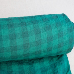 May include: A rolled-up bolt of fabric featuring a green and black plaid pattern. The fabric is a vibrant teal color with a darker green grid design. The material appears soft and possibly linen or cotton.