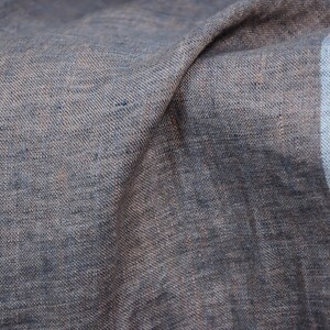 May include: Close-up of a textured, blue and brown fabric with a frayed edge. The fabric is folded and has a soft, natural look.