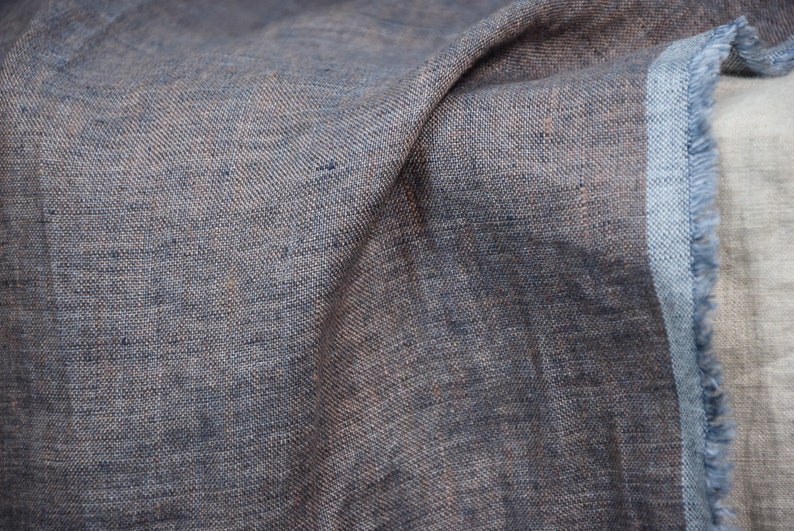 May include: Close-up of a textured, blue and brown fabric with a frayed edge. The fabric is folded and has a soft, natural look.