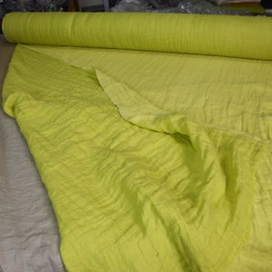 May include: A roll of light green fabric with a textured surface. The fabric is folded in half and the roll is lying on a table.