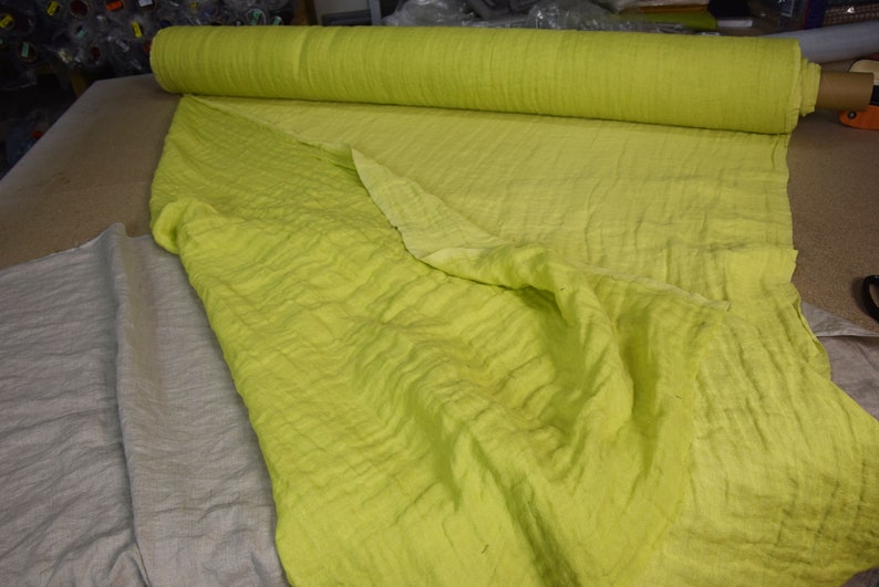 May include: A roll of light green fabric with a textured surface. The fabric is folded in half and the roll is lying on a table.