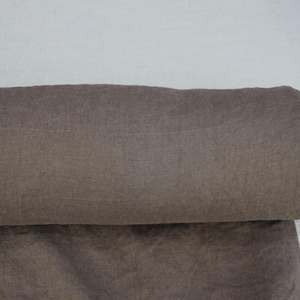 May include: A roll of brown fabric, partially unrolled, revealing a textured surface. The fabric is a muted shade of brown, with a slight sheen. The roll is resting on a light-colored surface.