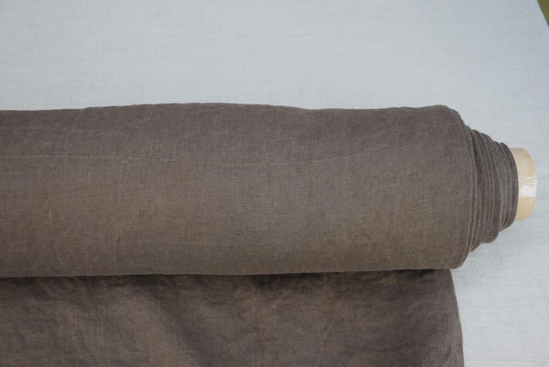 May include: A roll of brown fabric, partially unrolled, revealing a textured surface. The fabric is a muted shade of brown, with a slight sheen. The roll is resting on a light-colored surface.