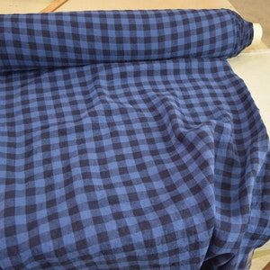 K&ouml;nnte beinhalten: Blauer und schwarzer Gingham-Stoff mit gewebter Struktur. Der Stoff ist gefaltet und aufgerollt.