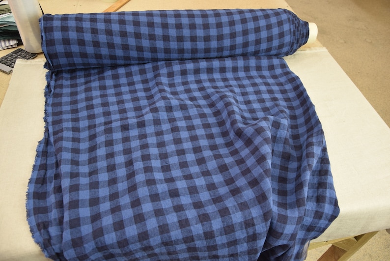 K&ouml;nnte beinhalten: Blauer und schwarzer Gingham-Stoff mit gewebter Struktur. Der Stoff ist gefaltet und aufgerollt.