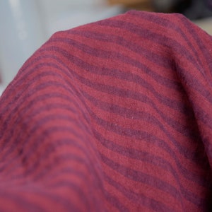 May include: Close-up of a burgundy fabric with a dark burgundy zebra stripe pattern.