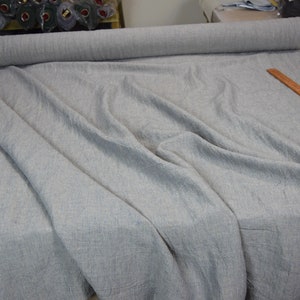 Puede incluir: Un rollo de tela gris claro con un sutil patr&oacute;n de rayas blancas. La tela est&aacute; colocada sobre una mesa con una regla de madera y unas tijeras.