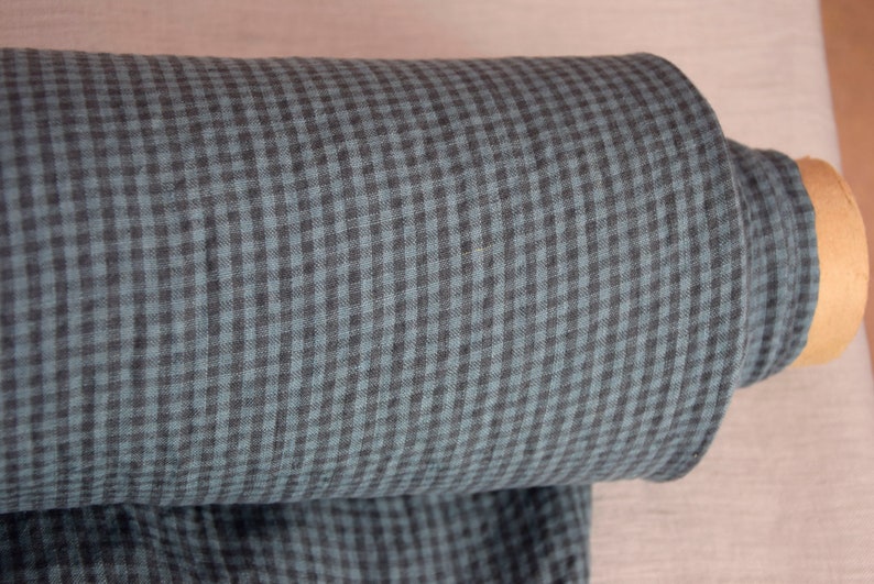 May include: A roll of fabric featuring a teal and black gingham pattern. The fabric is tightly rolled, revealing the pattern's repeating squares. The roll's core is a light brown cardboard tube.