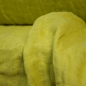 May include: A close-up of a yellow fabric with a textured weave. The fabric is folded and draped, creating soft folds and wrinkles.