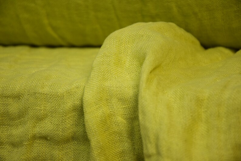 May include: A close-up of a yellow fabric with a textured weave. The fabric is folded and draped, creating soft folds and wrinkles.