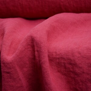 May include: Close-up of a deep pink linen fabric with a textured weave. The fabric is folded and draped, showcasing its soft and natural texture.