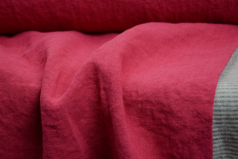 May include: Close-up of a deep pink linen fabric with a textured weave. The fabric is folded and draped, showcasing its soft and natural texture.