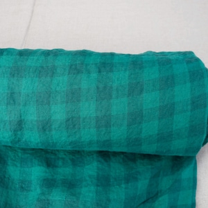 May include: A roll of teal and dark teal plaid fabric. The fabric is rolled up, revealing the pattern and texture. The fabric is likely linen or a similar material, suitable for clothing or home decor projects.