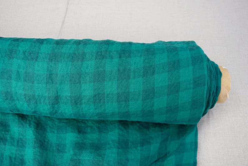 May include: A roll of teal and dark teal plaid fabric. The fabric is rolled up, revealing the pattern and texture. The fabric is likely linen or a similar material, suitable for clothing or home decor projects.