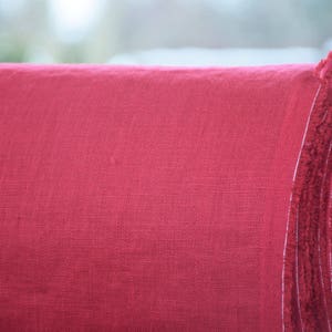 May include: Close-up of a roll of red linen fabric. The fabric has a textured, woven appearance.